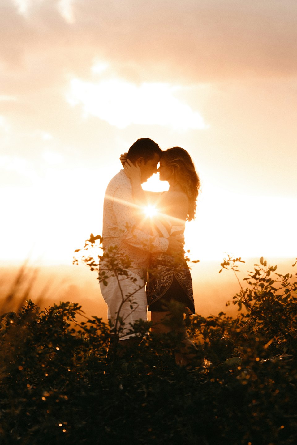 Couple embracing at sunset with sunbursts.