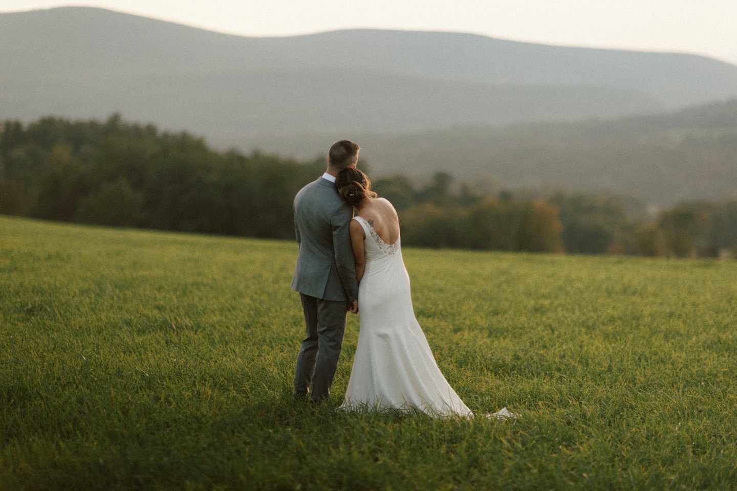 Newlyweds embrace in a green field overlooking hills.