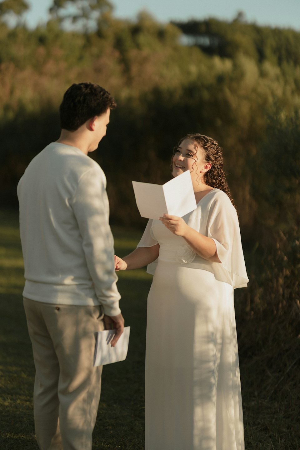 A couple holds hands and reads vows in a field.