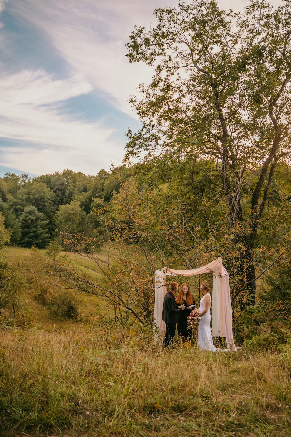 A couple exchanges wedding vows under a floral arch.