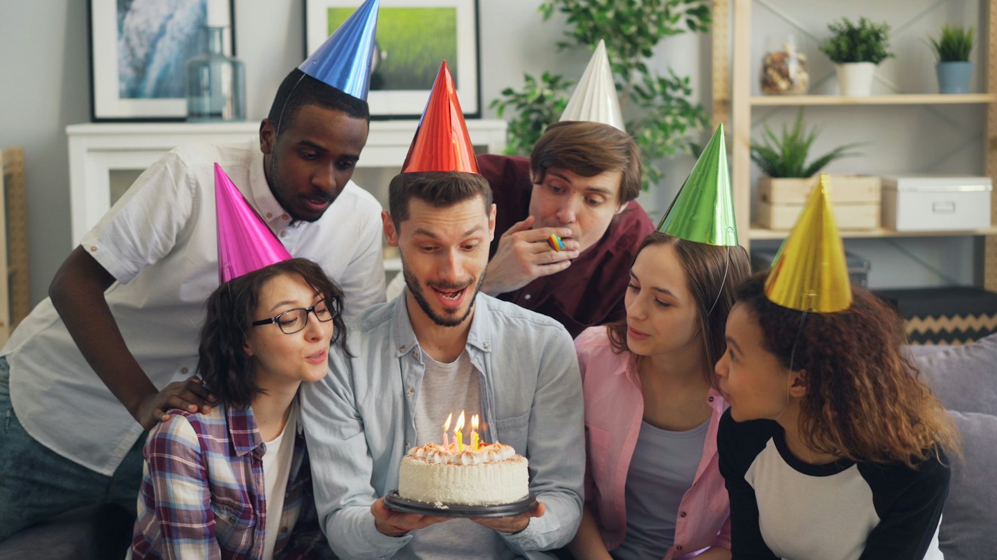 Group of friends celebrating a birthday with a lit cake.