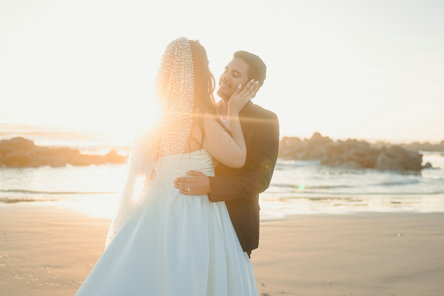 A bride and groom embrace on a sandy beach.